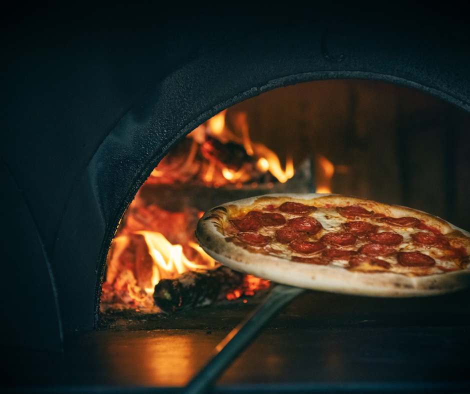 Wood-fired pizza emerging from the oven